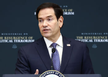 Marco Rubio, wearing a suit and patterned blue tie, speaks at a podium with a sign reading Ministerial on the Resurgence of Political Terrorism and a Department of State seal in front of a dark backdrop. He spoke about leftist terrorism.