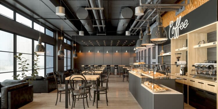 A coffee shop interior with wooden tables, a coffee maker, pastries, and pendant lights.