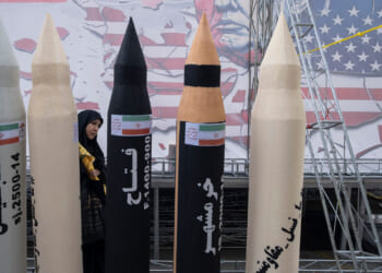 An Iranian woman walks behind mock-ups of four Iranian missiles against a backdrop of an drawing of a scowling Donald Trump.