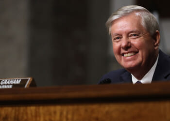 A smiling Lindsey Graham sits in a Senate hearing.
