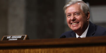 A smiling Lindsey Graham sits in a Senate hearing.