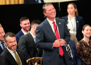 U.S. Rep. Ronny Jackson (R-TX) March 20, 2026 stands laughing amid a group of seated individuals.