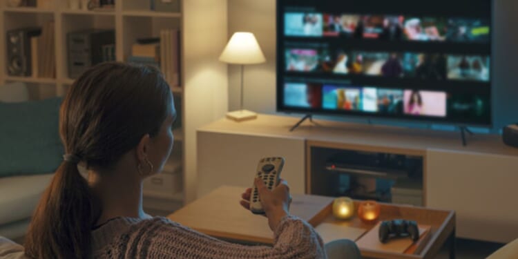 A young woman turns on the television in her living room.