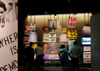 Visitors stand in front of an exhibit of protests signs at National Museum of American History.