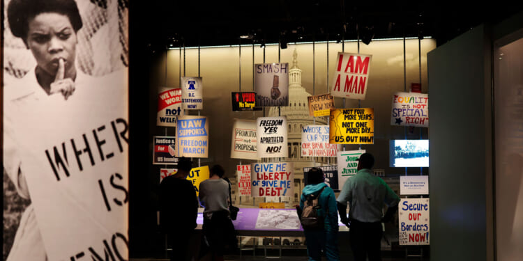 Visitors stand in front of an exhibit of protests signs at National Museum of American History.
