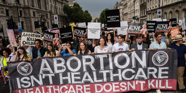 Pro-life protesters holding a sign: "Abortion Isn't Healthcare. Healthcare doesn't kill."