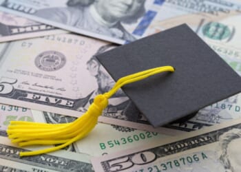 A graduation cap sits on a pile of money.