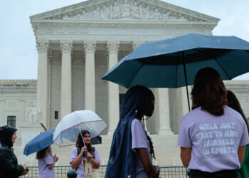 A group of young women stand around the Supreme Court with umbrellas.
