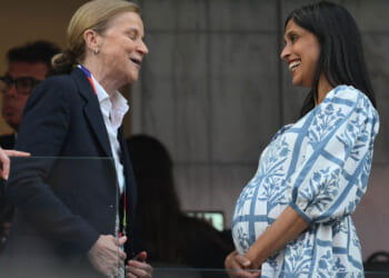A very pregnant Usha Vance in a white and blue dress speaks to someone at a World Cup match.