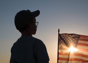 Silhouette of a boy with a setting sun shining through an American flag.