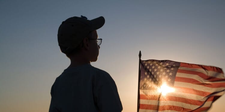 Silhouette of a boy with a setting sun shining through an American flag.