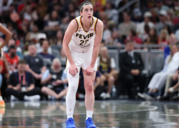Caitlin Clark rests her hands on her thighs in the middle of a basketball court.
