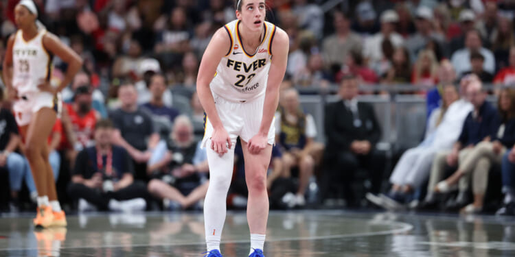 Caitlin Clark rests her hands on her thighs in the middle of a basketball court.