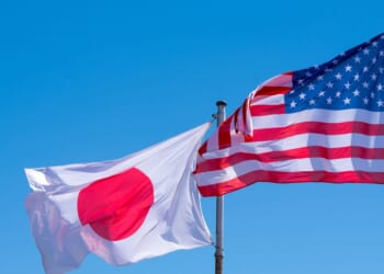 American and Japanese flags waving against a blue sky.