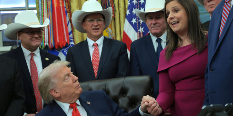Donald Trump holds hands with Rep. Elise Stefanik (R-NY) in the Oval Office with other officials gathered around.