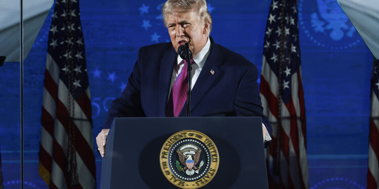 Trump stands at a podium with the presidential seal, speaking into a microphone about the dangers of communism. Multiple American flags are displayed behind him against a blue backdrop.