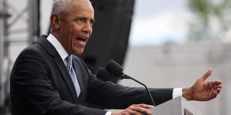 Barack Obama at a podium speaking with arm outstretched.