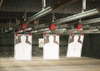 Indoor gun range targets hang from a bar on the ceiling.