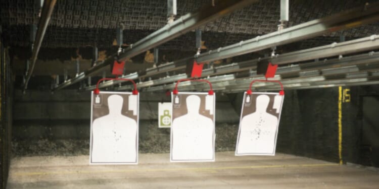 Indoor gun range targets hang from a bar on the ceiling.