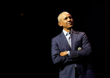 Barack Obama, with his arms folded, against a black background.