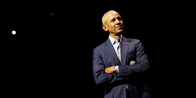 Barack Obama, with his arms folded, against a black background.