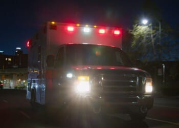 An ambulance driving through a downtown district at night.