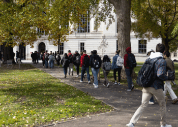 College students with backpacks walk along a tree-lined Ohio campus path on a sunny day with fallen leaves on the ground.