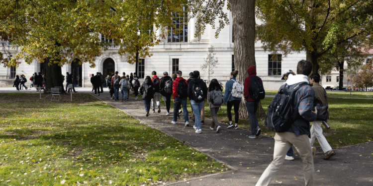College students with backpacks walk along a tree-lined Ohio campus path on a sunny day with fallen leaves on the ground.