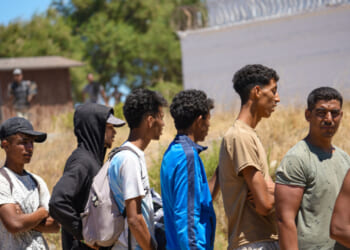 A group of migrants stands in line at El Trampolin beach in Ceuta, Spain, on August 2, 2026, to drink water and fill their bottles from a Spanish Army water truck. People wait to receive drinking water during a humanitarian assistance operation near the coast. (Photo by Ana Lopez/NurPhoto via Getty Images)