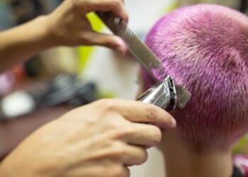 A female hairdresser giving a hairstyle to a young woman with pink dyed short hair.