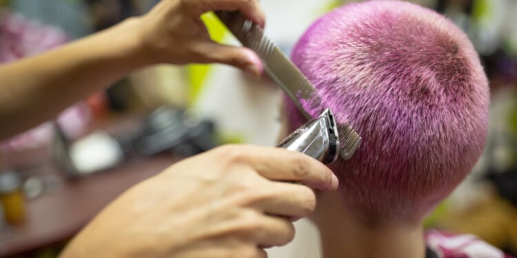 A female hairdresser giving a hairstyle to a young woman with pink dyed short hair.