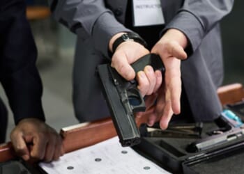 A man with a gun instructs another man nearby in a safety training session.