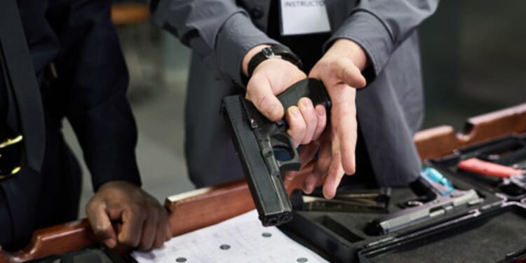 A man with a gun instructs another man nearby in a safety training session.