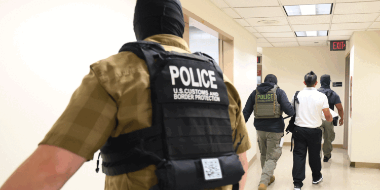 Several officers, including U.S. Customs and Border Protection, escort two individuals down a hallway in a government building.