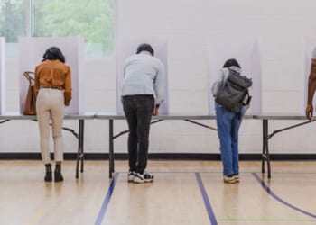 People line up at voting booths on Election Day in a school gym.
