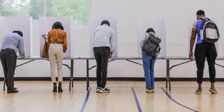 People line up at voting booths on Election Day in a school gym.