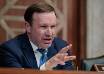 Sen. Chris Murphy's plan to increase the minimum wage would harm low-income workers, a study finds. Pictured: Murphy, a man in a blue suit speaks emphatically at a desk with a nameplate reading SEN. MUR visible, gesturing with his hand. The background shows a wooden panel and part of a marble wall.