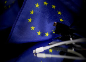 A picture taken on February 6, 2020 in Brussels shows plugs for mobile charger next to a European flag. - The European Parliament demanded that the EU urgently force tech companies to adopt a universal charger, setting up a clash with Apple and its widely used iPhone connector cable. (Photo by Kenzo TRIBOUILLARD / AFP) (Photo by KENZO TRIBOUILLARD/AFP via Getty Images)