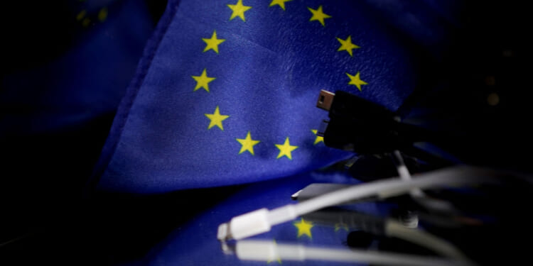 A picture taken on February 6, 2020 in Brussels shows plugs for mobile charger next to a European flag. - The European Parliament demanded that the EU urgently force tech companies to adopt a universal charger, setting up a clash with Apple and its widely used iPhone connector cable. (Photo by Kenzo TRIBOUILLARD / AFP) (Photo by KENZO TRIBOUILLARD/AFP via Getty Images)