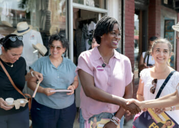 Angie Nixon in a short-sleeve pink shirt greets women while campaigning on a sidewalk.