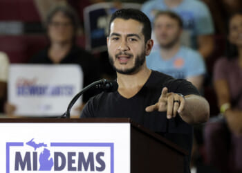 Michigan Democrat Abdul El-Sayed compared circumcision to transgender surgery. Pictured: El-Sayed, a man speaks at a podium labeled MIDEMS in front of an audience. He gestures with one hand while addressing the crowd. People in the background hold signs and appear to be listening attentively.