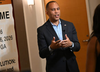 Hakeem Jeffries in suit speaks to a woman in front of a NABJ conference welcome sign in a hallway.