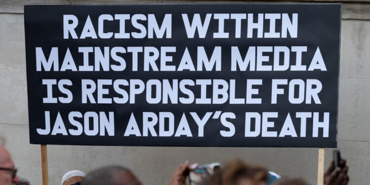 A black sign with white lettering holds "Racism within mainstream media is responsible for Jason Arday's death."
