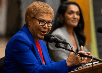 Mayor Karen Bass, wearing a blue blazer, speaks into a microphone while her hands are at a podium.