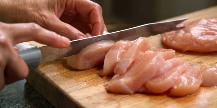 A close-up shot of a woman cutting raw chicken.
