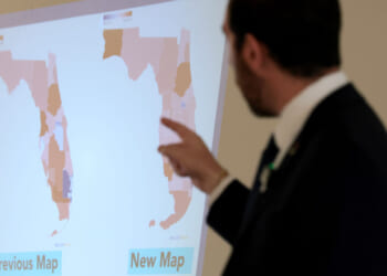 A person in a suit points at a screen displaying two maps of Florida labeled Previous Map and New Map, showing different district boundaries.