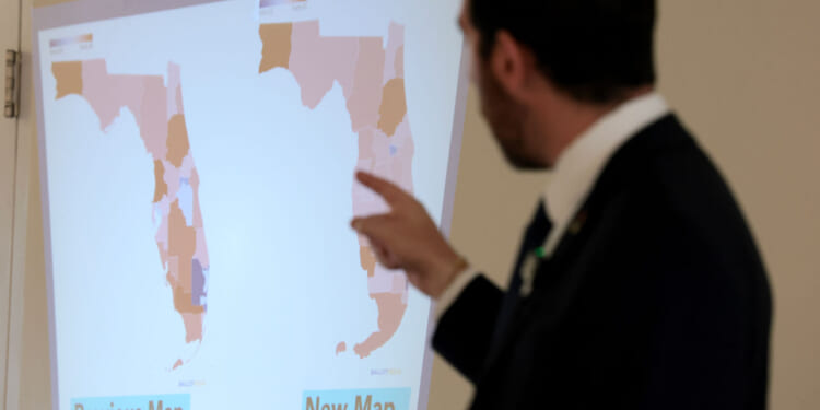 A person in a suit points at a screen displaying two maps of Florida labeled Previous Map and New Map, showing different district boundaries.