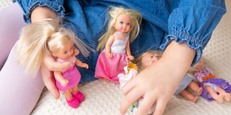 A young girl plays with female toy dolls on her bed.