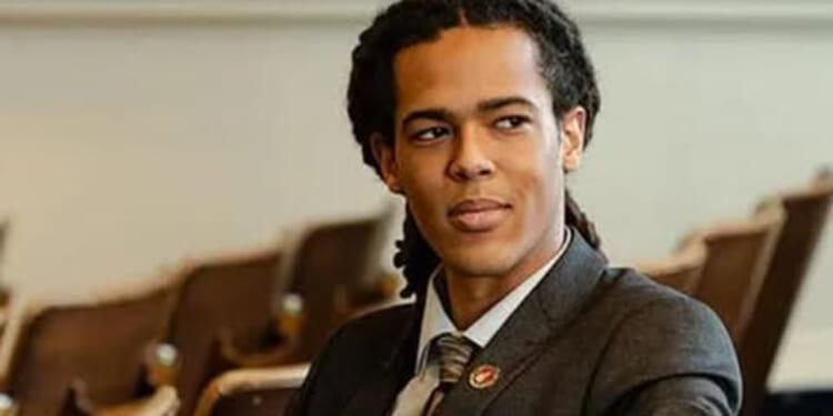 Democrat Jonah Wheeler is not afraid to buck his party on transgender orthodoxy and gender ideology. Pictured: Wheeler, a man with long, dark hair in dreadlocks, wearing a suit and tie, sits in an auditorium with brown seats, looking to the side.