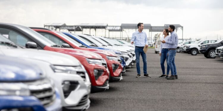 A young couple looks at cars on a car dealership lot.